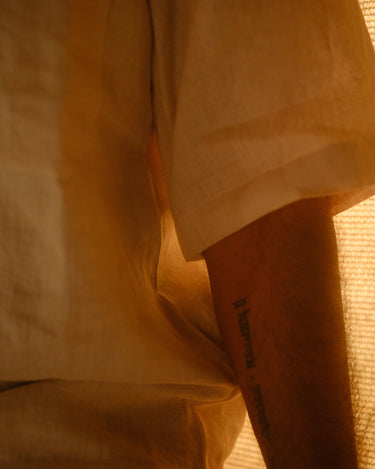 Close up of the half sleeve detail of an off-white linen shirt worn by a man in a soft light