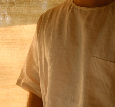 A man in offwhite pure linen t-shirt featuring a left pocket standing in soft light