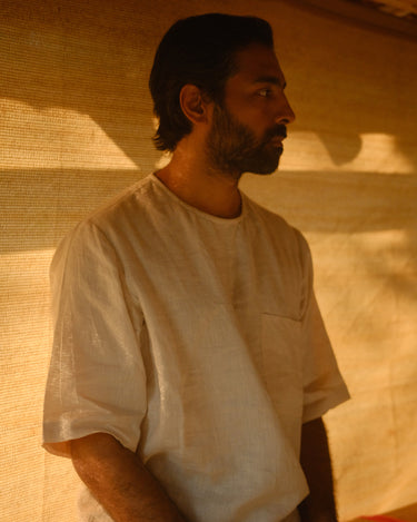 a man in off-white linen t-shirt sitting on a wooden bench