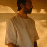 a man in off-white linen t-shirt sitting on a wooden bench