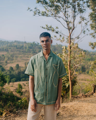 man in  Green fish hand-embroidered  linen shirt standing on a hill top overlooking a valley. Half sleeve shirt, Material: linen