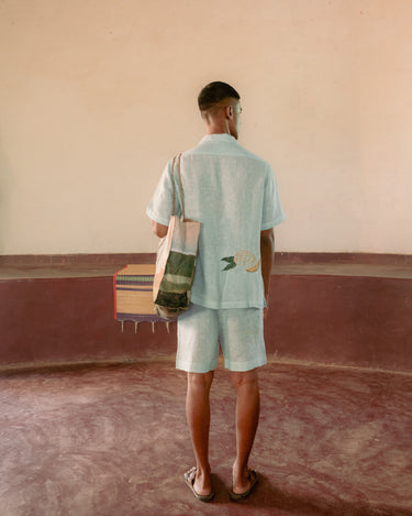 Detailed back view of a man in a yoga hall wearing green and white stripes linen co-ordinated set of shirt and shorts with embroidered mango.