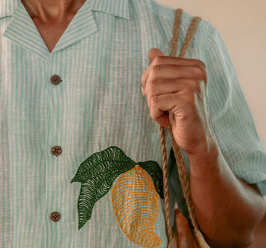 a man wearing  green and white stripe linen shirt with embroidered mangoes. Detailed view