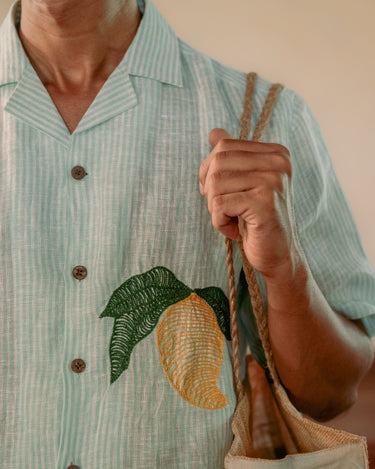 a man wearing  green and white stripe linen shirt with embroidered mangoes. Detailed view