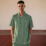 man in eco-friendly Green fish hand-embroidered  linen shirt standing in a yoga hall. Half sleeve shirt, Material: linen, Front view