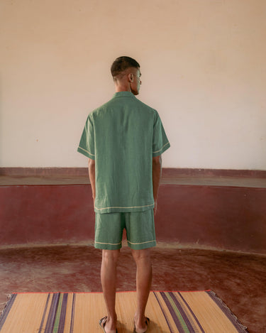 back view of a man in a green hand-embroidered  linen shirt standing in a yoga hall. Half sleeve shirt, Material: linen, Back view