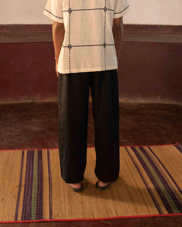 A man standing in a yoga hall wearing black linen lounge pants. Back view