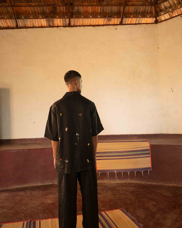 A man in eco-friendly, wild sprigs hand-embroidered linen shirt in a yoga hall. half sleeves shirt, Material: linen, back view