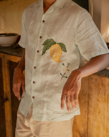 a detailed view of a man wearing green and white stripes linen shirt with embroidered mangoes.